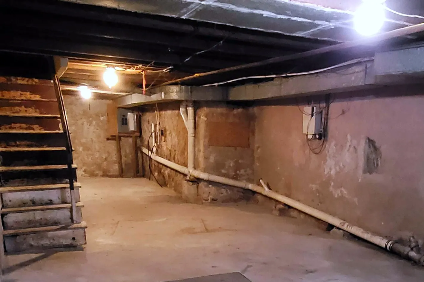 The same basement before, with stone walls, a bare slab and an old wooden stair
