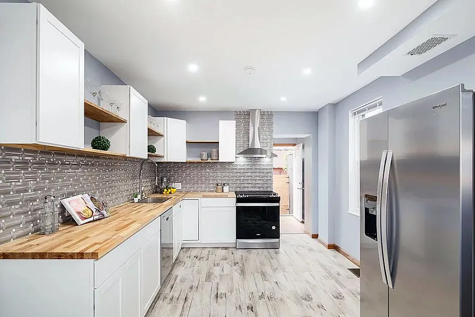 After: the kitchen from the dining side, from cherry cabinets and a white range to white shaker cabinets, butcher block and a stainless range