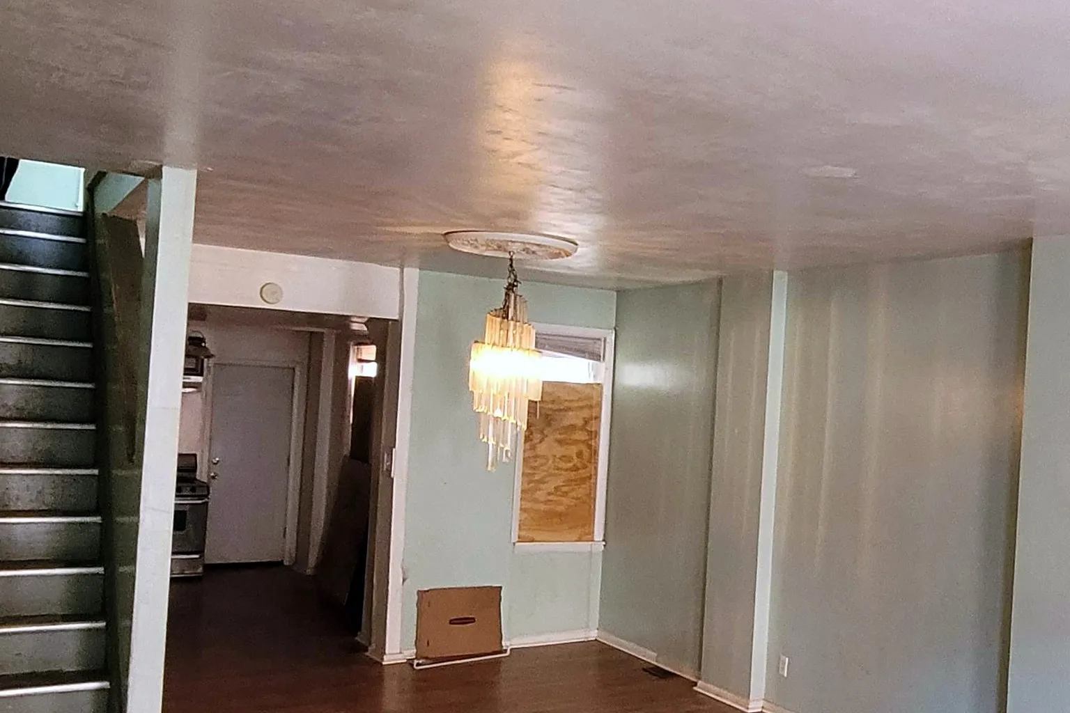 Living room before, with patched plaster walls and a boxed-in stair