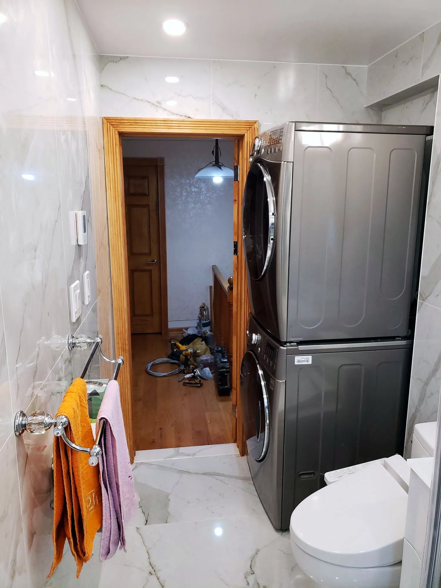 Compact bathroom with marble-look porcelain floor and wall tile and a stacked laundry