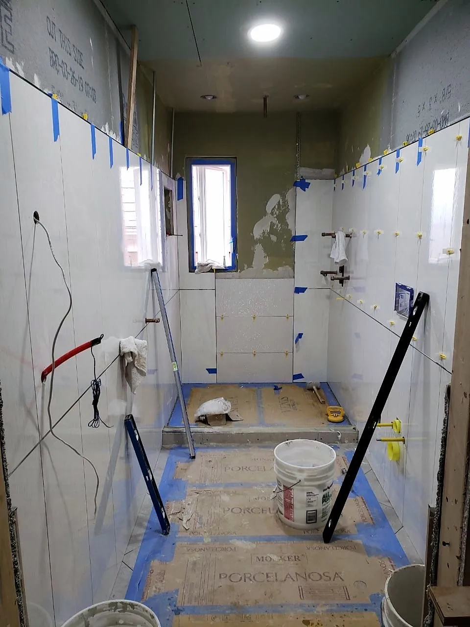 Large-format tile being set on bathroom walls with blue tape and spacers