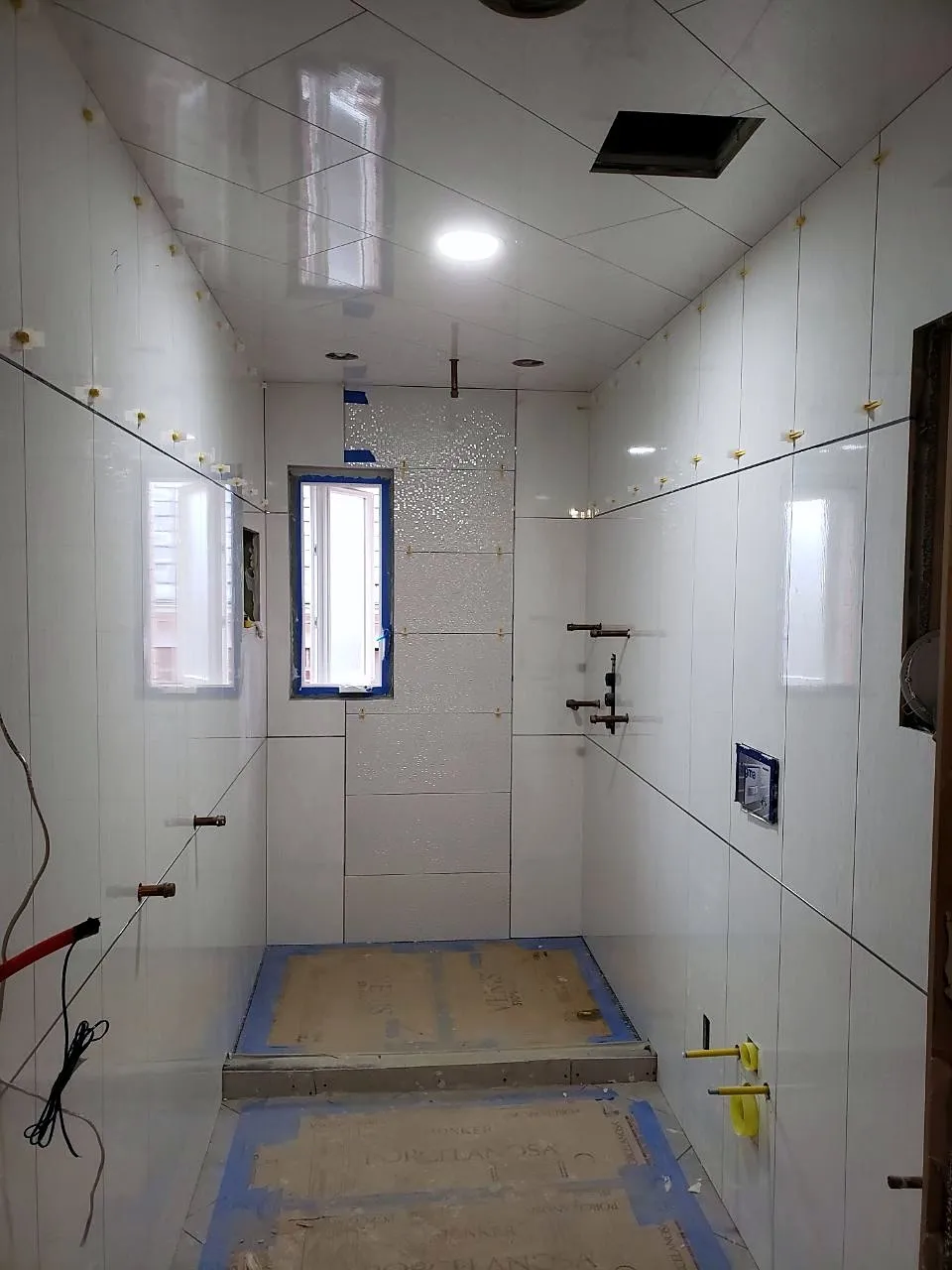 Bathroom walls tiled in white large-format porcelain with leveling clips before grout