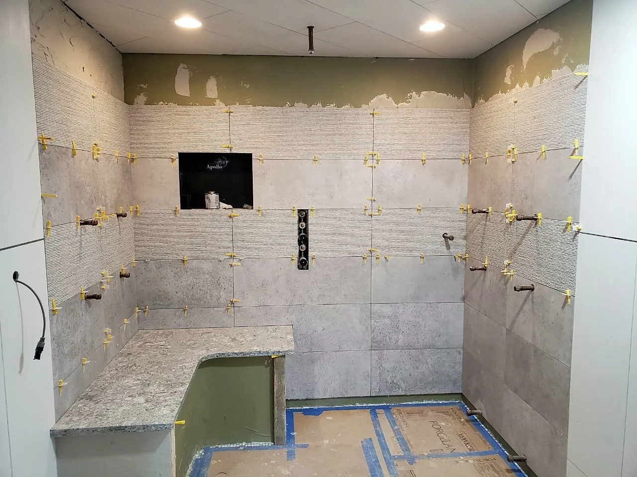 Grey linear porcelain being set on a shower wall with leveling clips