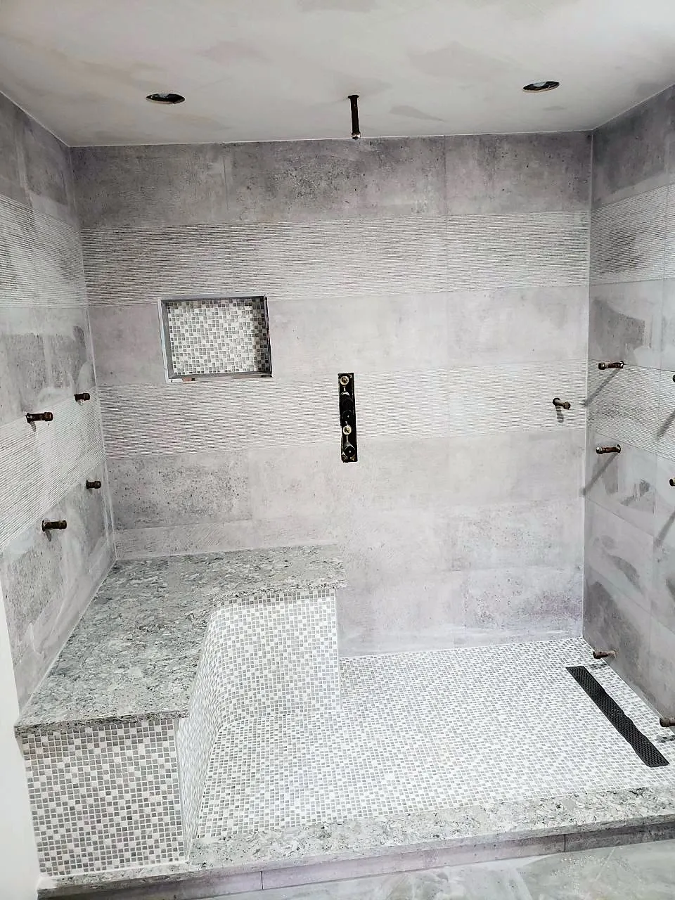 Walk-in shower with a tiled bench, recessed niche, linear drain and pebble floor