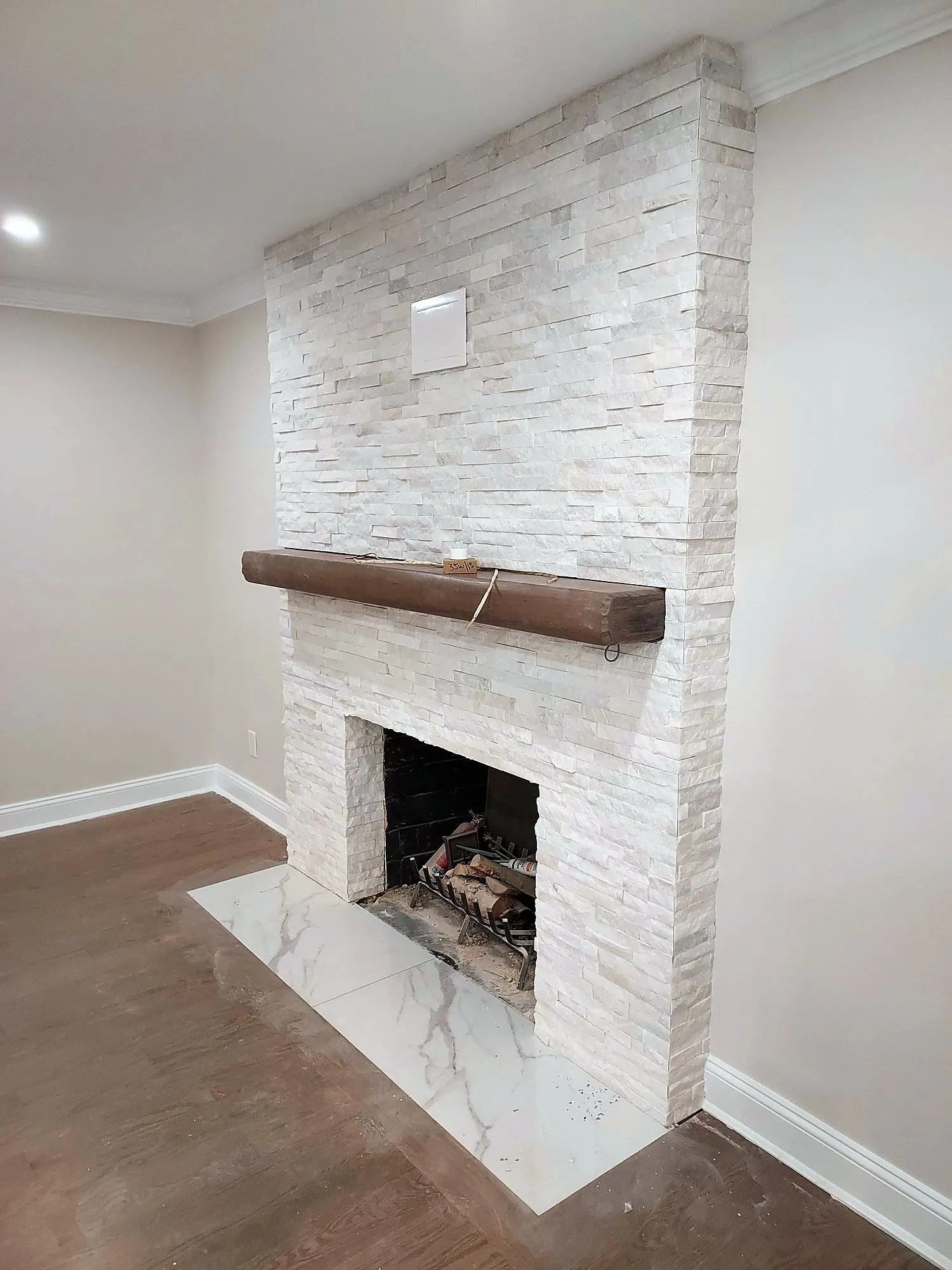 Floor-to-ceiling white stacked-stone fireplace with a dark wood mantel and marble hearth