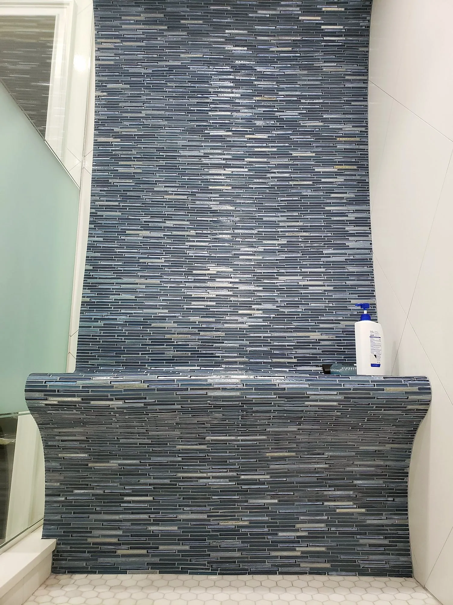 Curved blue glass mosaic feature wall in a small Queens bathroom with white large-format tile beside it
