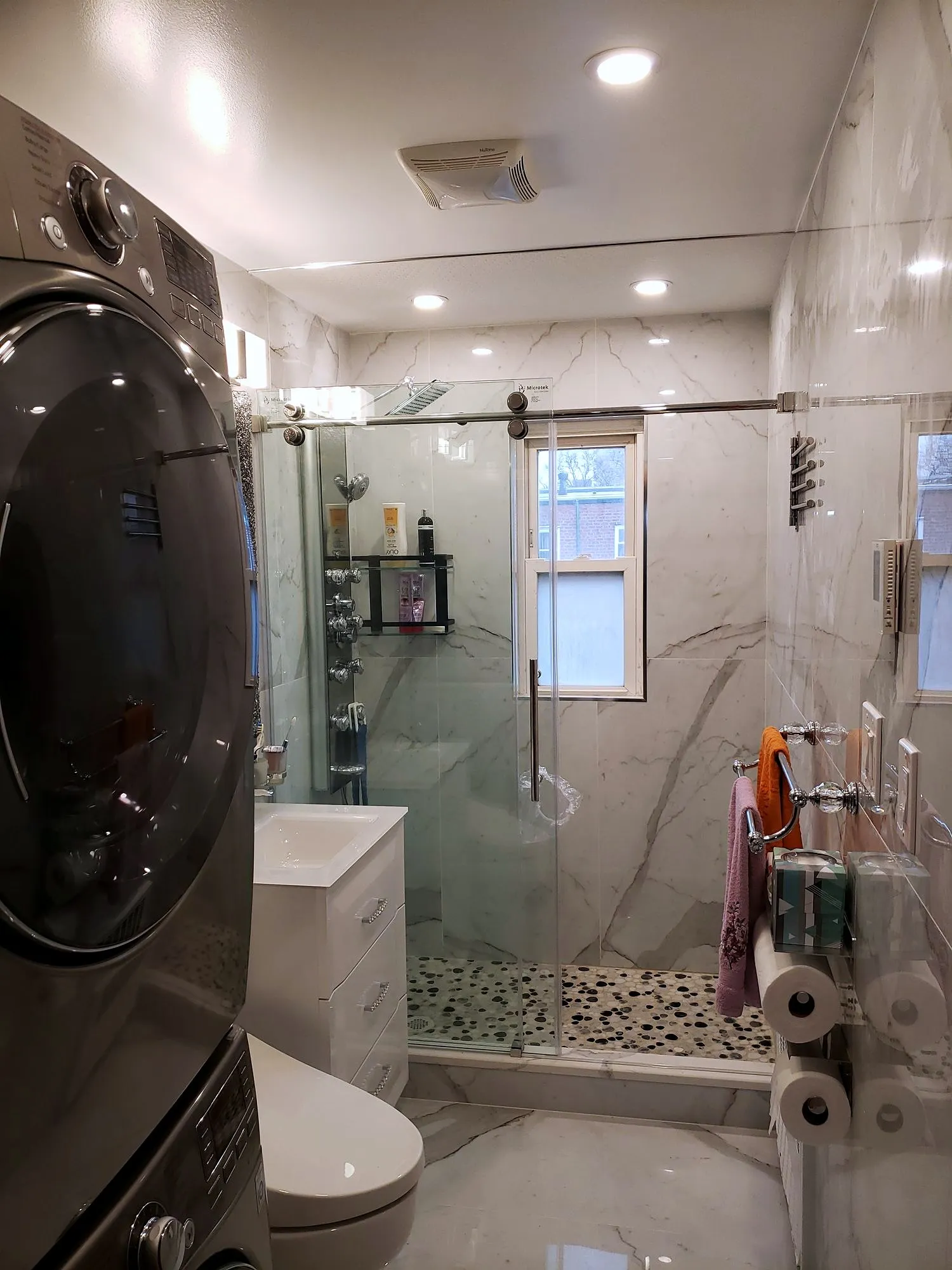 Finished compact bathroom with marble-look porcelain, frameless glass shower and a stacked washer and dryer