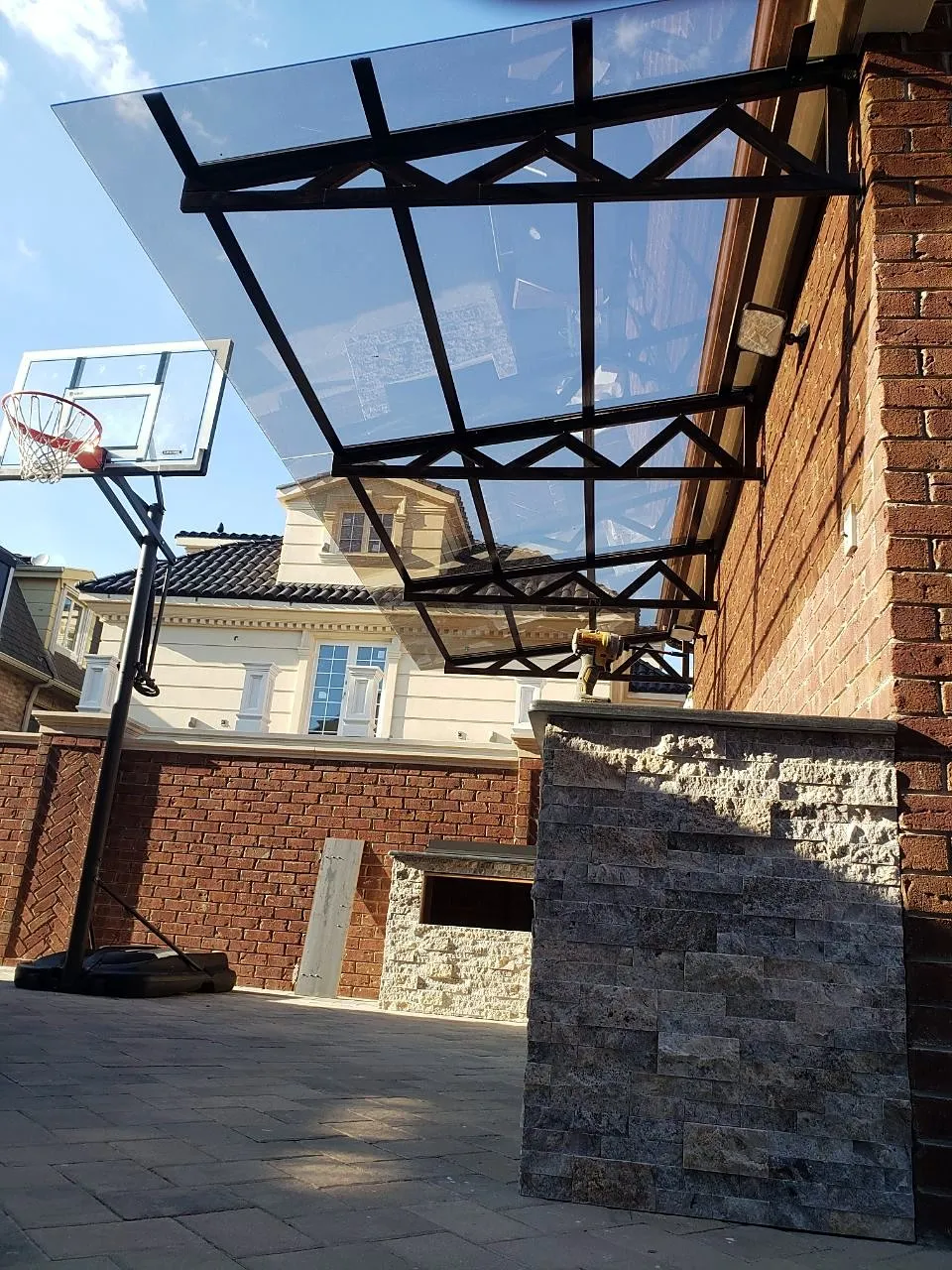 Steel canopy frame with glass roof over a brick and stone outdoor bar