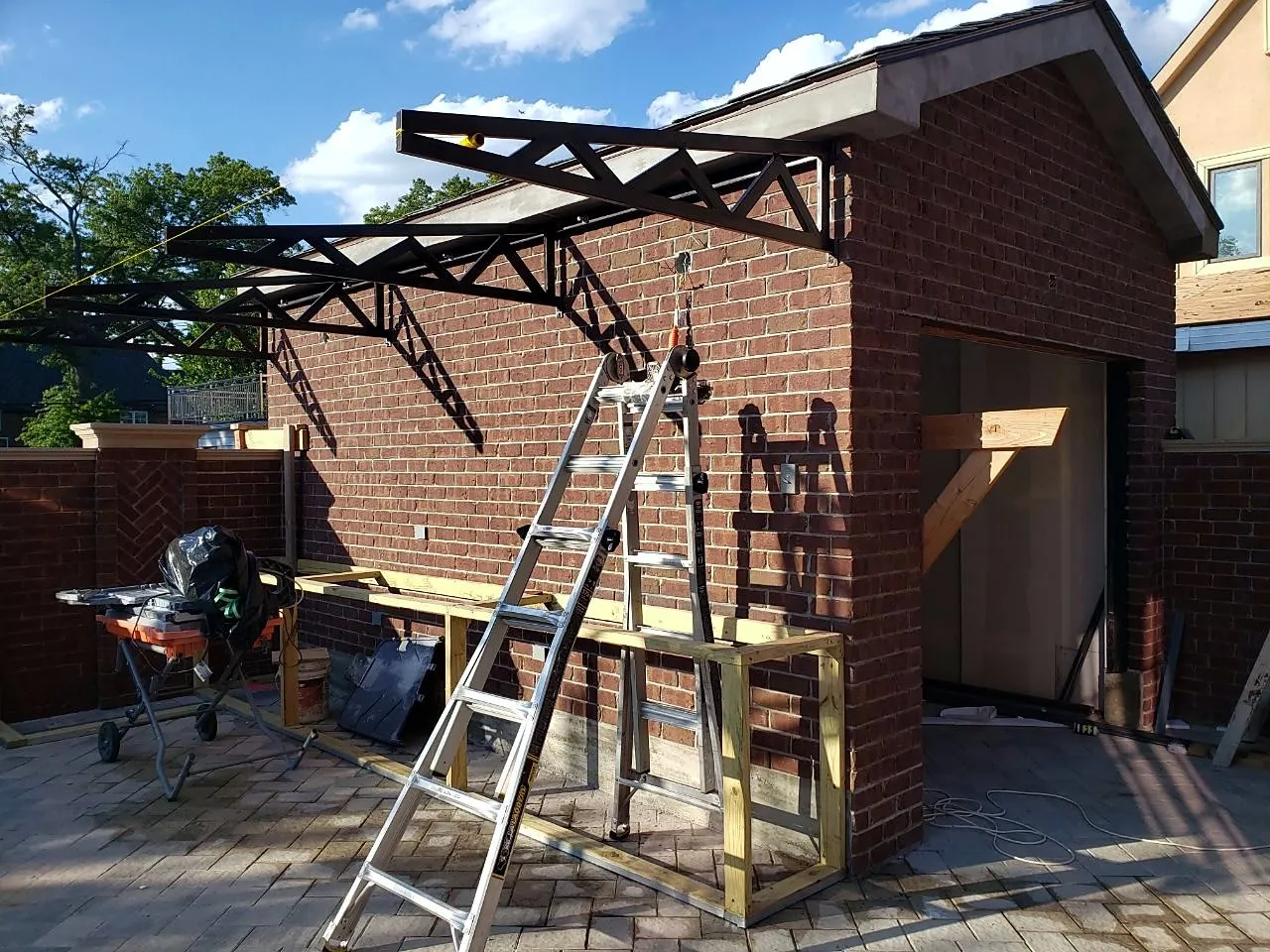Steel canopy being installed next to the garage with a ladder in place