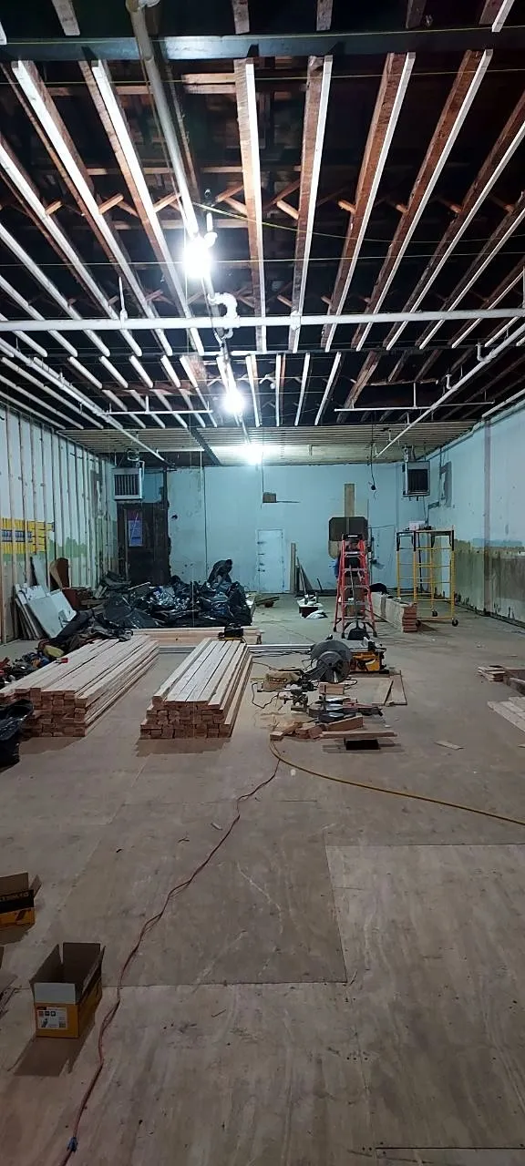 Ceiling framing in progress with work lights in a long commercial space