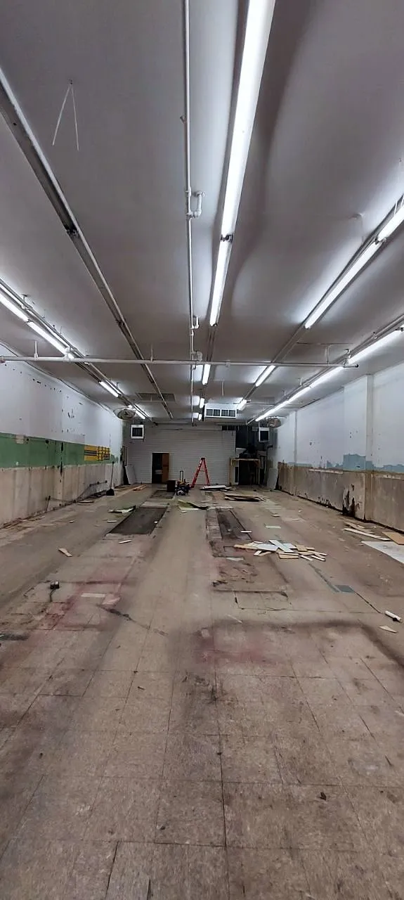 Empty commercial space with fluorescent lights and bare floor before work