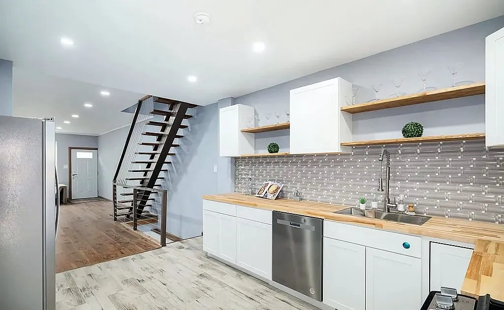 Renovated rowhouse kitchen with white shaker cabinets, butcher-block counters and an open-tread staircase