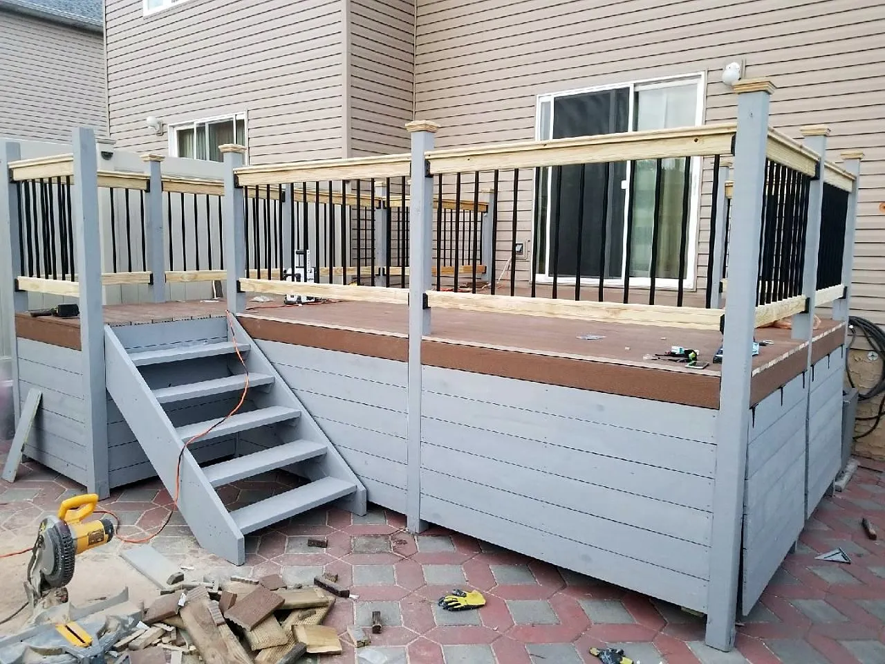 Finished raised composite deck with white railings, skirting and a side stair onto a paver patio
